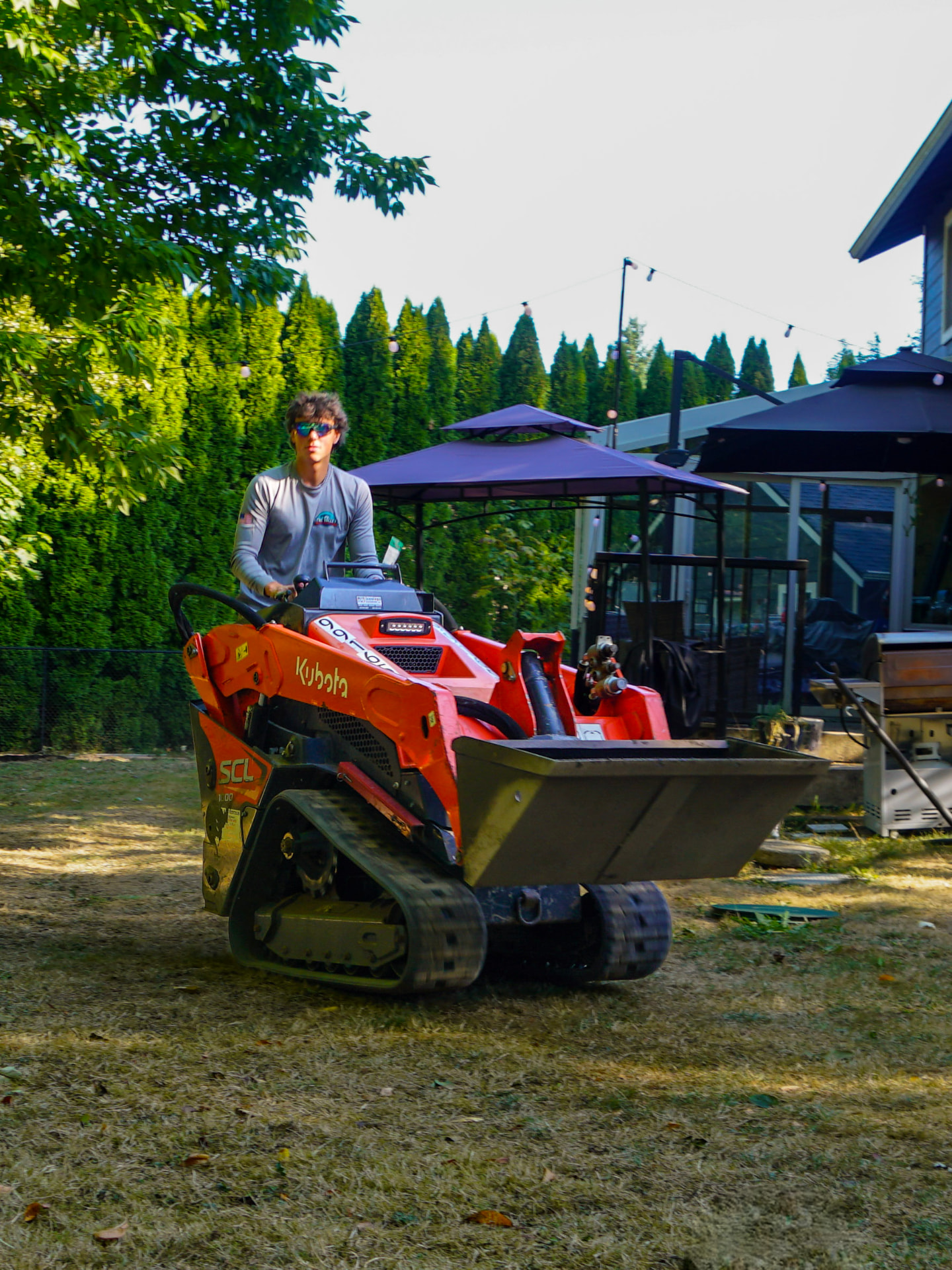 Crew member operating a compact track loader in a customer's yard